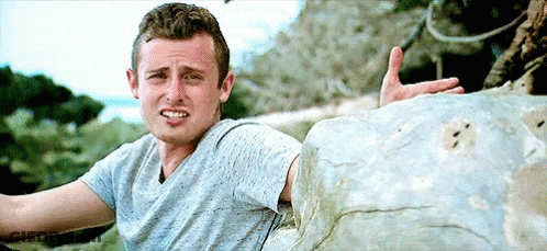 Man In Blue Shirt Sitting On Rock Making Face GIF
