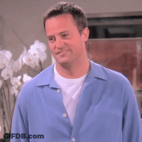 Man In Blue Shirt Smiling In Front Of Flowers GIF
