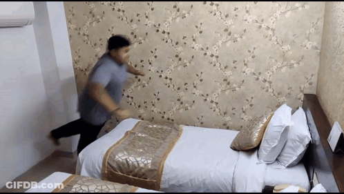 Man In Blue Shirt Standing In Front Of Bed GIF