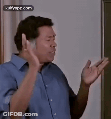 Man In Blue Shirt Standing In Front Of Blackboard Making Funny Face GIF