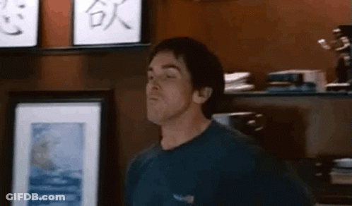 Man In Blue Shirt Standing In Front Of Shelf With Picture GIF