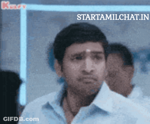 Man In Blue Shirt Standing In Front Of Startamilchat.in Sign GIF
