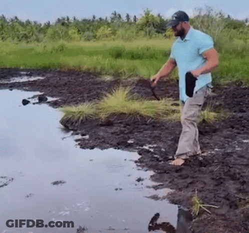 Man In Blue Shirt Standing In Muddy Field Near River GIF