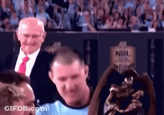 Man In Blue Shirt Standing Next To Trophy In Stadium GIF