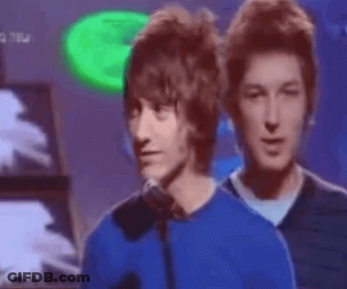 Man In Blue Shirt Talking Into Microphone With Two Men Looking On GIF