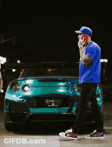 Man In Blue Shirt Talking On Cell Phone In Front Of Green Car GIF