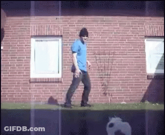 Man In Blue Shirt Walking In Front Of Brick Wall GIF