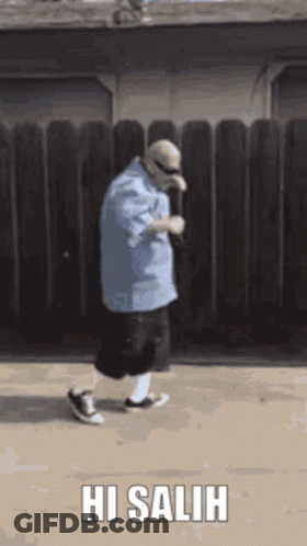 Man In Blue Shirt Walking In Front Of Wooden Fence Saying Hi Salih GIF