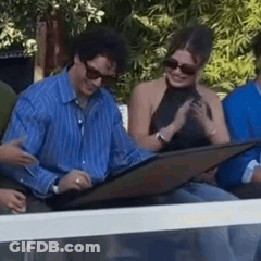 Man In Blue Striped Shirt Sitting Next To Woman With Sunglasses GIF