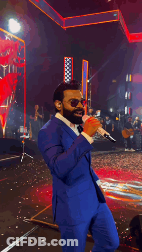 Man In Blue Suit And Mask Singing On Stage GIF