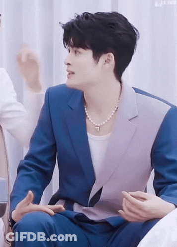 Man In Blue Suit And Pearl Necklace Talking To Another Man GIF