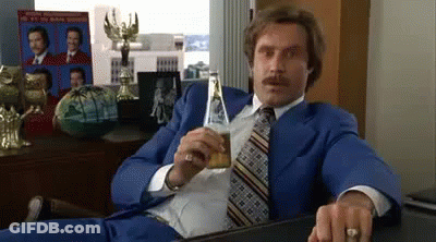 Man In Blue Suit Holding Beer At Desk GIF