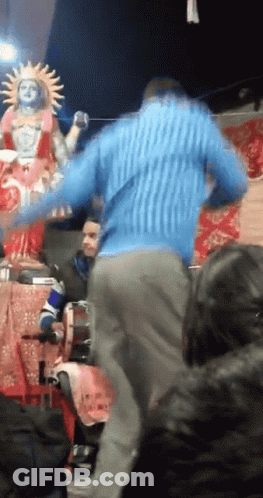 Man In Blue Sweater Dancing In Front Of Sun Statue GIF