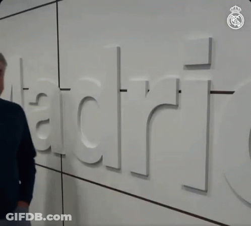 Man In Blue Sweater In Front Of Wall Saying Madrid GIF
