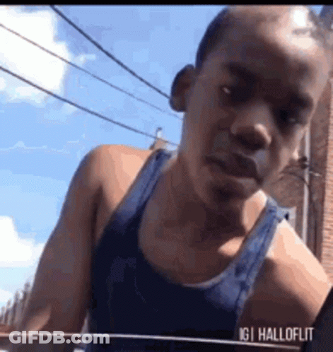 Man In Blue Tank Top In Front Of Brick Building GIF