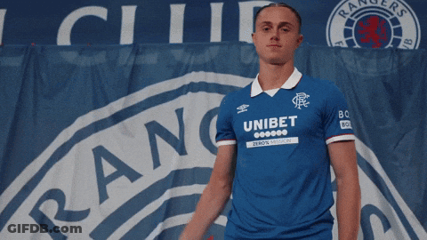 Man In Blue Unibet Shirt In Front Of Rangers Banner GIF
