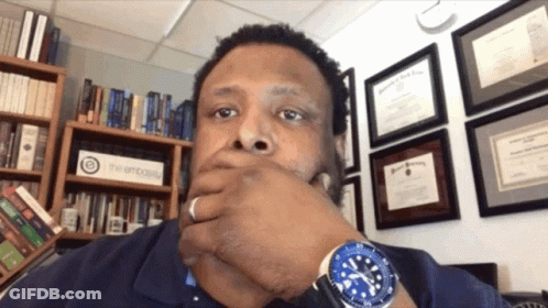 Man In Blue Watch In Front Of Bookshelf Saying The Embassy GIF