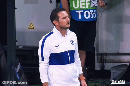 Man In Blue White Nike Jacket In Front Of Man In Green Vest Saying UEF T035 GIF