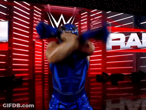 Man In Blue Wrestling Outfit With Raw On Red Wall GIF