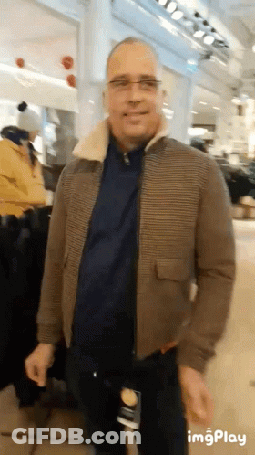 Man In Brown Jacket And Glasses Standing In Store GIF