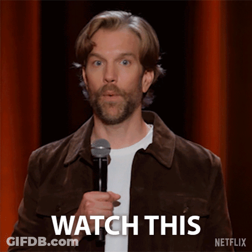 Man In Brown Jacket Holding Microphone Saying Watch This GIF