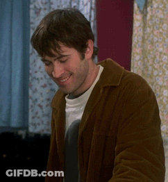 Man In Brown Jacket Smiling In Front Of Window GIF