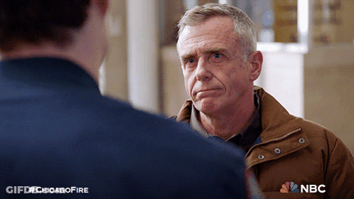 Man In Brown Jacket Talking To Man In Blue Shirt NBC Logo GIF