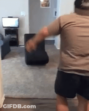 Man In Brown Shirt Standing In Living Room With Chair GIF