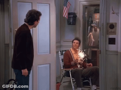 Man In Brown Sweater Next To Man Holding Sparkler GIF