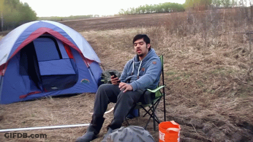 Man In Chair In Front Of Tent With Fire Bucket GIF