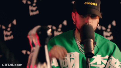 Man In Chomp Hat And Green Shirt Singing Into Microphone GIF