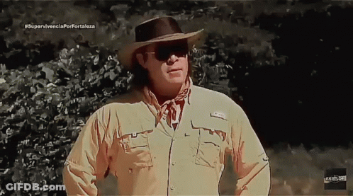 Man In Cowboy Hat And Sunglasses In Front Of Supervivencia Porfortaleza Sign GIF