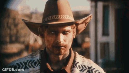 Man In Cowboy Hat And Sweater In Front Of Building GIF