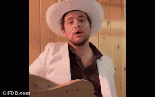 Man In Cowboy Hat And White Jacket Holding Guitar GIF