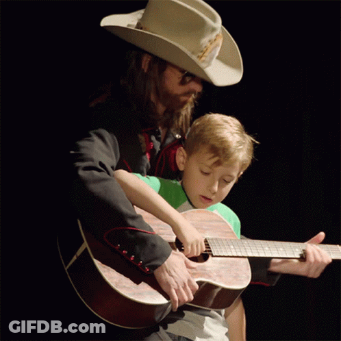Man In Cowboy Hat Helping Boy Play Guitar GIF