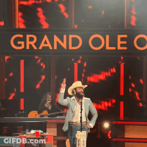 Man In Cowboy Hat On Stage With Grand Oleo Sign GIF