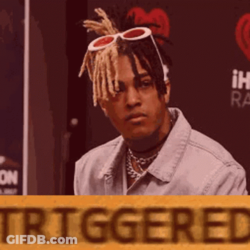 Man In Denim Jacket And Sunglasses Sitting In Front Of Triggered Sign GIF