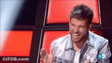 Man In Denim Jacket Laughing By Red Couch GIF