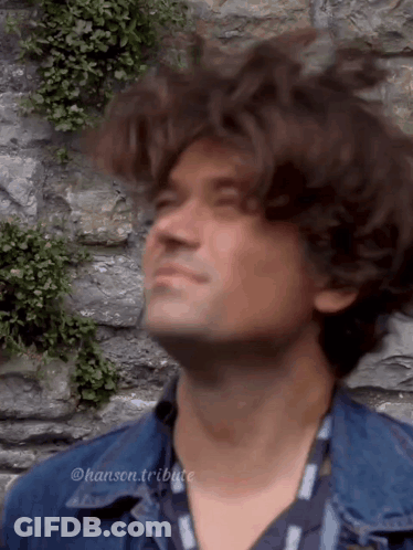 Man In Denim Jacket Looking Up At Stone Wall GIF