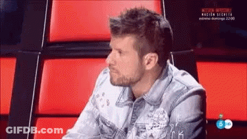 Man In Denim Jacket Sitting In Chair With Red Cushions GIF