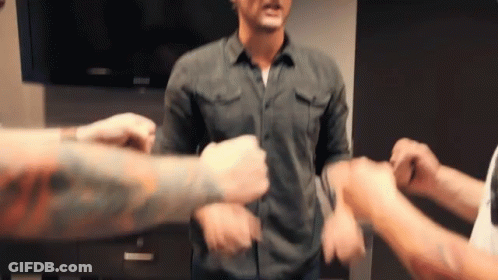 Man In Denim Shirt Surrounded By Hands GIF