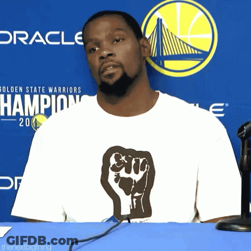Man In Fist T-Shirt In Front Of Warriors Logo GIF