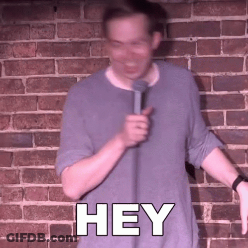 Man In Front Of Brick Wall Holding Microphone Saying Hey GIF