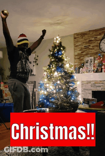 Man In Front Of Christmas Tree With Word Christmas Below GIF