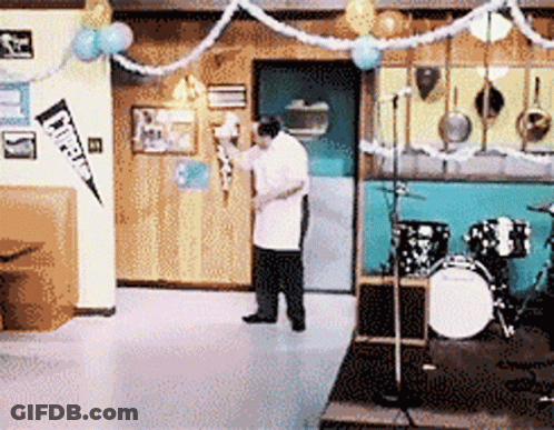 Man In Front Of Drum Set With Cheerleader Pennant GIF