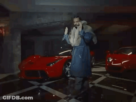 Man In Fur Coat Next To Two Red Sports Cars GIF