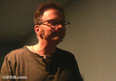 Man In Glasses And Grey Shirt In Dark Room GIF