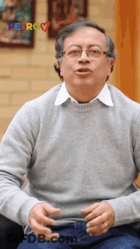 Man In Glasses And Grey Sweater Sitting By Petro Sign GIF
