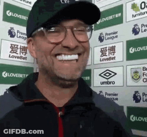 Man In Glasses And Hat Smiling In Front Of Lovebet Signs GIF
