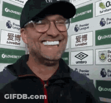 Man In Glasses And Hat Smiling In Front Of Umbro Logos GIF